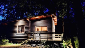 Une cabane avec deux fenêtres, une véranda et une petite terrasse.