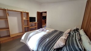 Ein Schlafzimmer mit einem Bett, gestreifter Bettwäsche, einem Holzschrank und einem Fernseher auf einem Regal.