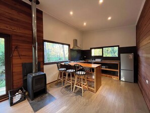 Une cuisine compacte dotée d’un îlot central, de chaises en bois, d’une cuisinière encastrée et d’un réfrigérateur.