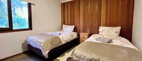 Un dormitorio con dos camas, paneles de madera en la pared, una ventana y una mesita de noche.