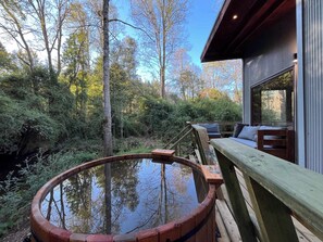 Une terrasse en bois avec un jacuzzi, donnant sur une zone boisée.