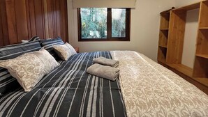 A bedroom with a bed, wooden paneling on the wall, a window with a view of trees, and a wooden wardrobe. - Oak Cabin - Hot Tub, BBQ, WiFi & Riverside (Huiscapi)