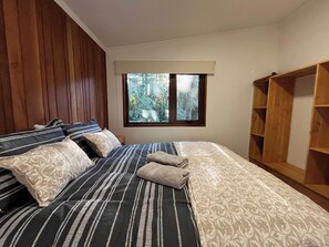 Une chambre à coucher avec un lit, un lambris en bois sur le mur, une fenêtre donnant sur des arbres et une armoire en bois.