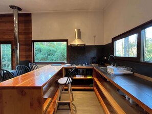 Eine moderne Küche mit einer Holztheke, Barhocker, einem großen Fenster und Blick auf den Wald.