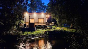 Eine Holzhütte mit einer Terrasse, umgeben von Bäumen und einem kleinen Teich.