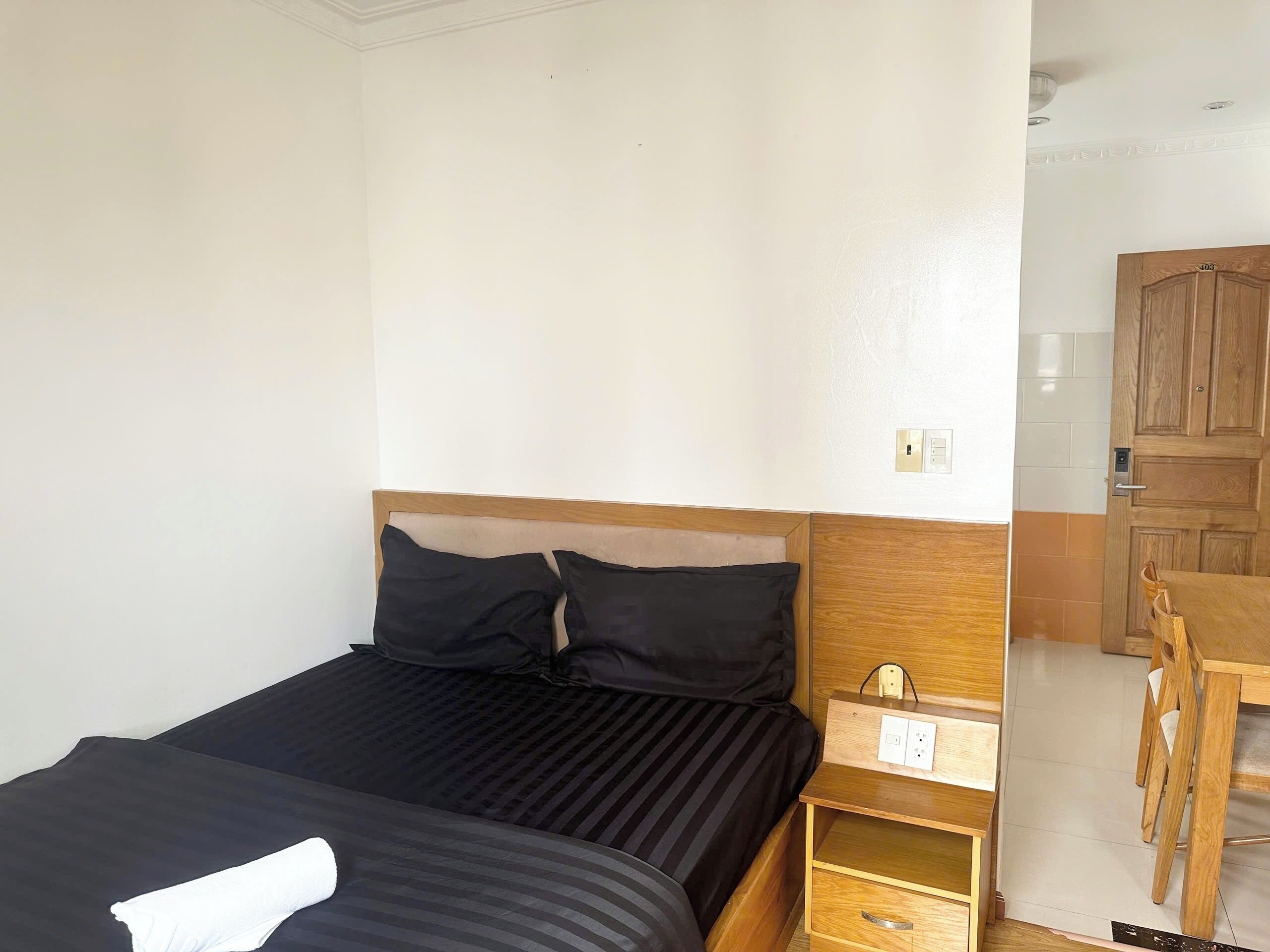 A hotel room with a bed, a wooden nightstand, a desk, and a wardrobe.