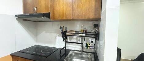 Une cuisine compacte dotée de meubles en bois, d’un plan de travail noir, d’un évier en acier inoxydable et d’une plaque de cuisson à induction intégrée.
