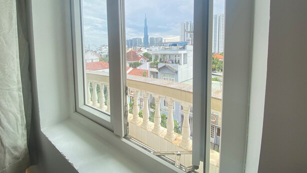 A window with a view of a cityscape, including a prominent skyscraper. - Uhouse - KELLY Thao Dien Apartment (Ho Chi Minh City)