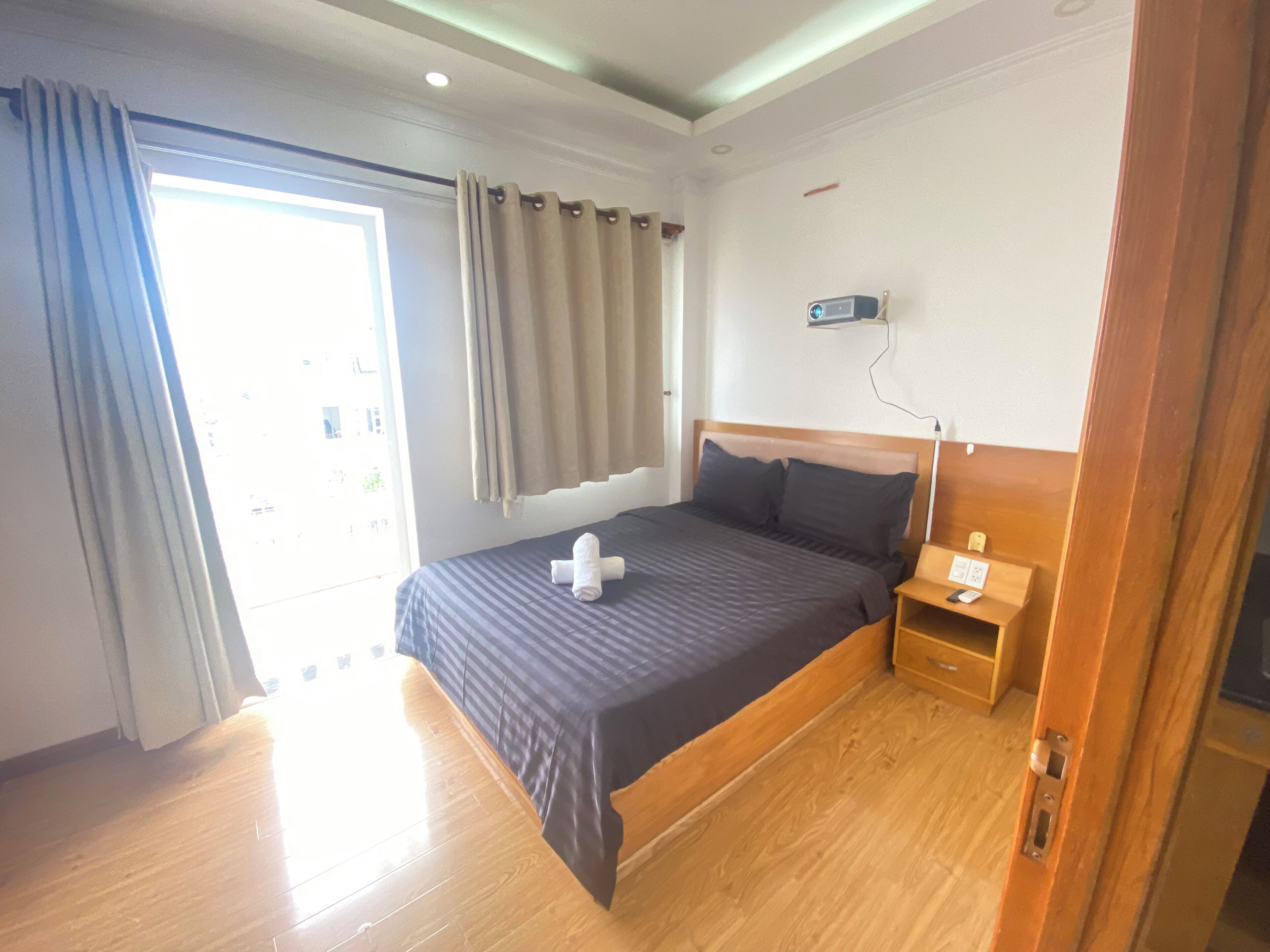 Ein Hotelzimmer mit einem großen Bett, Holzboden, einem Nachttisch mit Lampe und einem Vorhangfenster.