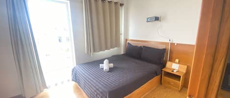 Ein Hotelzimmer mit einem großen Bett, Holzboden, einem Nachttisch mit Lampe und einem Vorhangfenster.