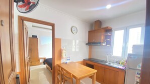 A compact kitchen with wooden cabinets, a dining table with chairs, a sink, and a refrigerator. - Uhouse - KELLY Thao Dien Apartment (Ho Chi Minh City)
