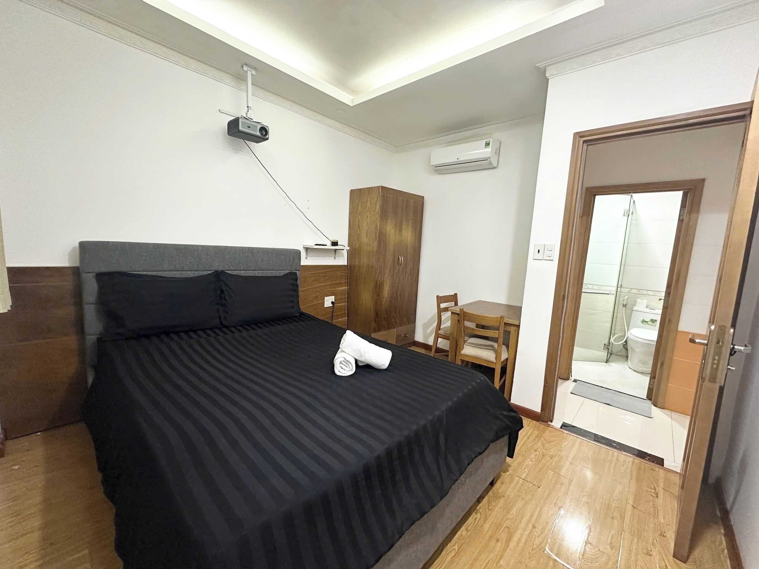 A hotel room with a bed, a desk, a chair, an air conditioning unit, and a door leading to a balcony.
