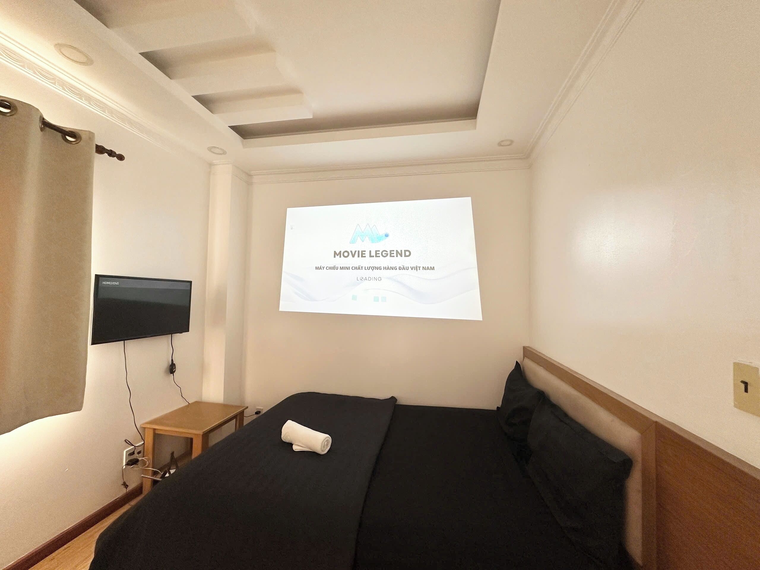 A hotel room with a bed, a TV mounted on the wall, and a poster on the wall.