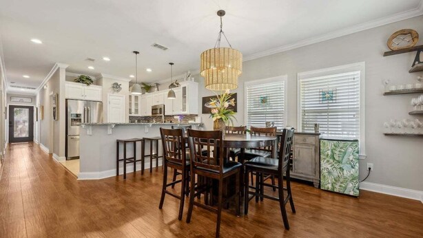 A modern kitchen with wooden flooring, a dining area with chairs, and pendant lighting.