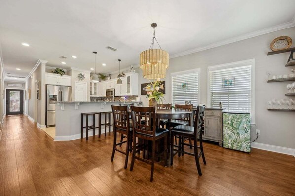 A modern kitchen with wooden flooring, a dining area with chairs, and pendant lighting.