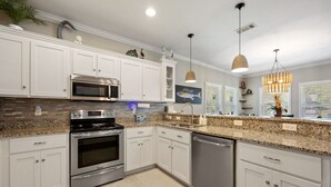 A modern kitchen with white cabinets, stainless steel appliances, granite countertops, and pendant lighting.