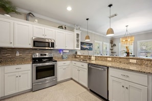 A modern kitchen with white cabinets, stainless steel appliances, granite countertops, and pendant lighting.
