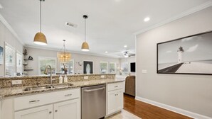 A modern kitchen with granite countertops, stainless steel appliances, pendant lighting, and a large framed picture of a lighthouse.