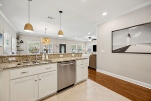 A modern kitchen with granite countertops, stainless steel appliances, pendant lighting, and a large framed picture of a lighthouse.