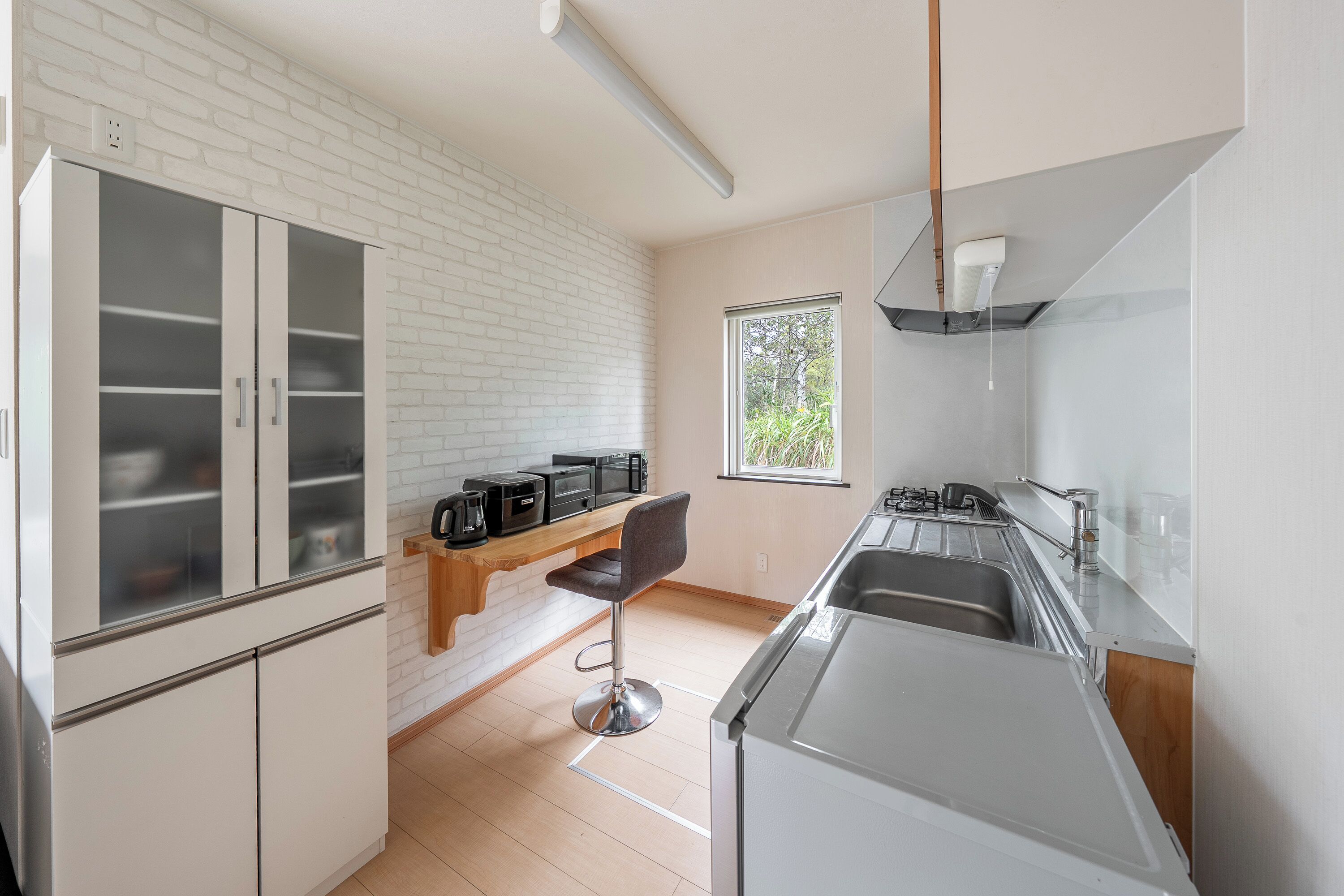 Une cuisine moderne avec des meubles blancs, un tabouret de bar et une fenêtre qui laisse entrer la lumière naturelle.