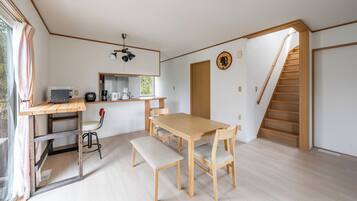 A spacious room with a wooden dining table, benches, and a kitchen area with a microwave and coffee maker.