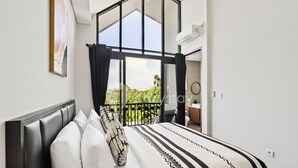 A bedroom with a large window, a bed with white bedding, and a view of greenery outside.
