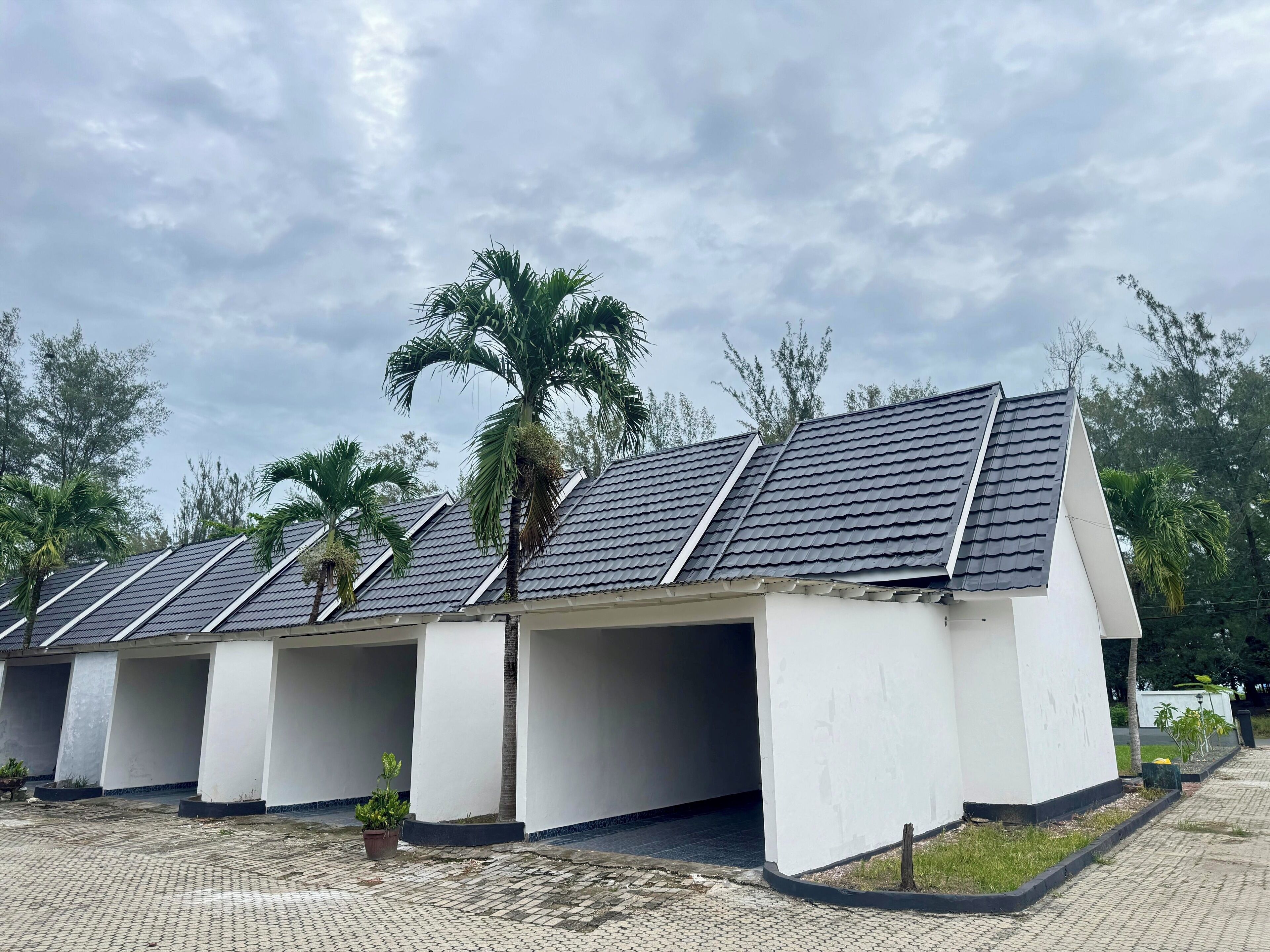 Una hilera de edificios blancos con techos oscuros, rodeados de palmeras y un área pavimentada.