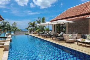 A pool area with lounge chairs and umbrellas, surrounded by palm trees and a stone wall.