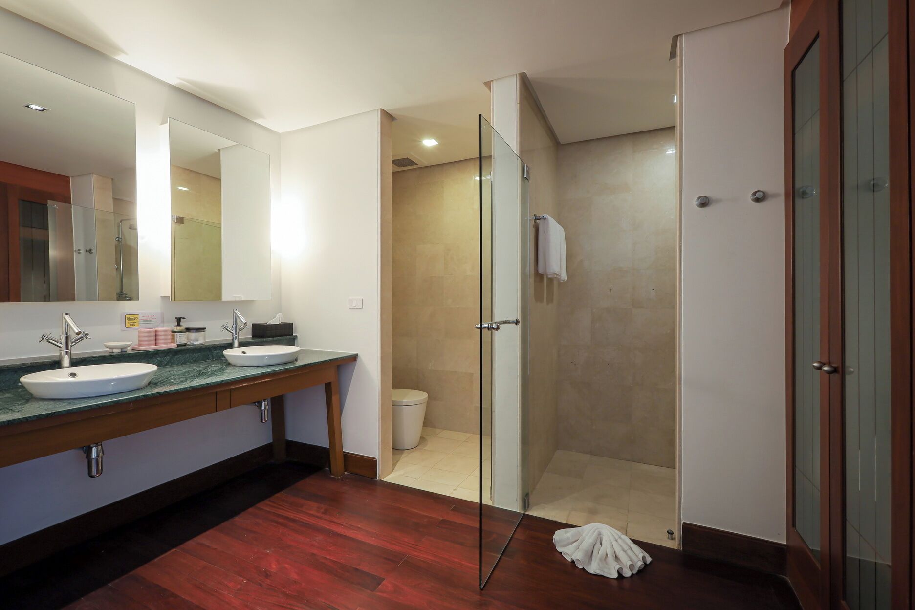Une salle de bain moderne avec un grand miroir, deux lavabos, une douche et un plancher en bois.