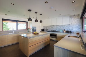 A modern kitchen with wooden cabinets, a central island, pendant lighting, and a tiled backsplash. -  Katamanda Villa Allegra 5BR Seaview villa Kata (Karon)