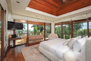 A bedroom with a large bed, a desk with a laptop, a TV, and a view of the outdoors. -  Katamanda Villa Allegra 5BR Seaview villa Kata (Karon)