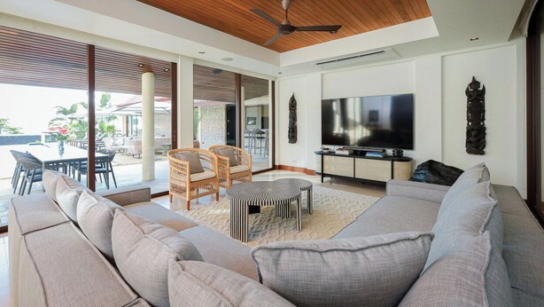 Ein modernes Wohnzimmer mit einer großen Couch, einem Essbereich mit Stühlen, einem Fernseher und einem Deckenventilator.