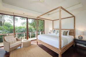 A four-poster bed with a wooden frame, a wicker chair, a small round ottoman, and a nightstand with a lamp. -  Katamanda Villa Allegra 5BR Seaview villa Kata (Karon)