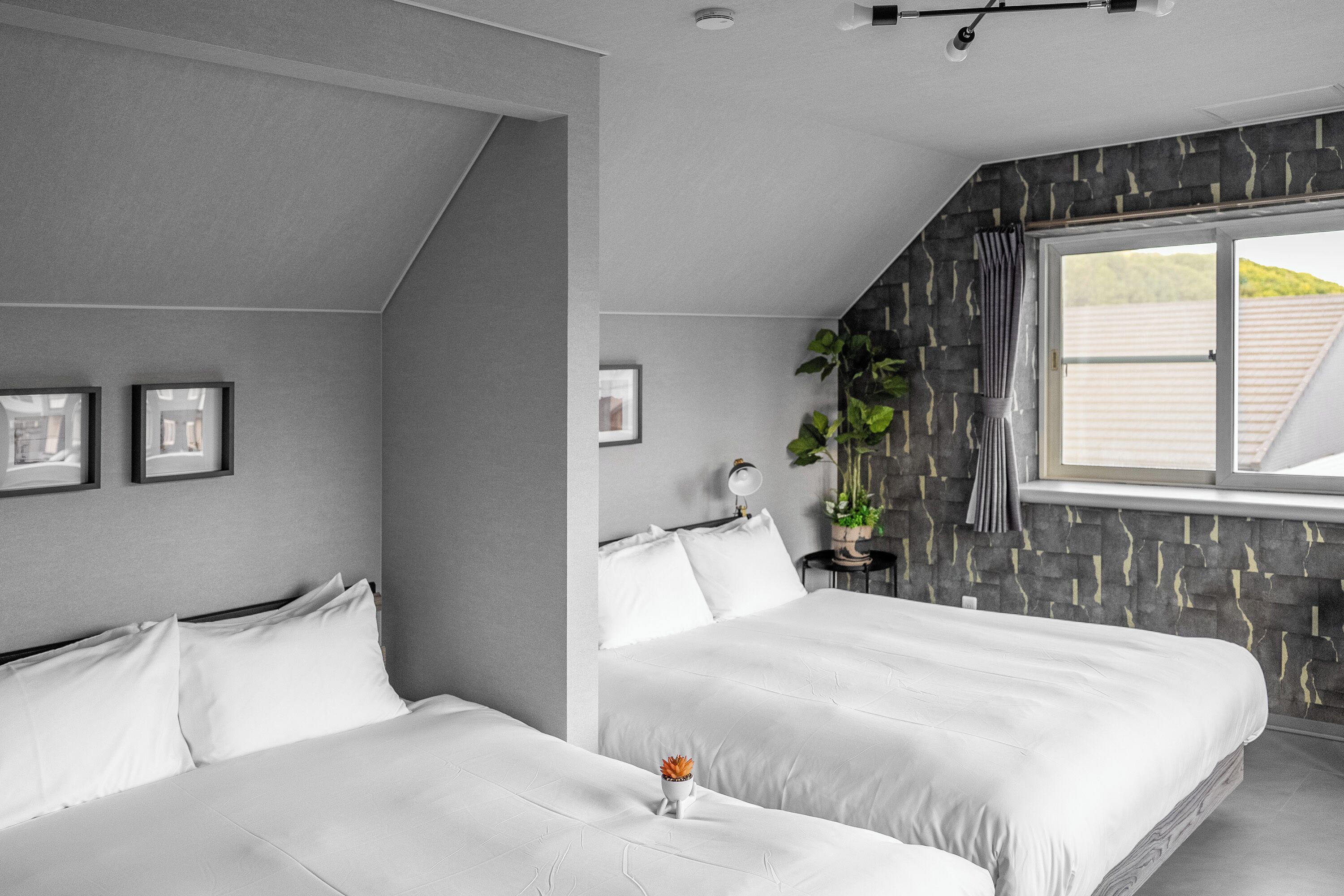 A modern bedroom with two beds, a stone accent wall, and a window with a view.