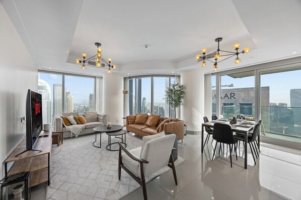 A spacious living area with a large window, a sofa, a dining table, and a TV.