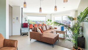 A spacious living room with a large brown leather sofa, orange chairs, and a dining area with a view of the city. - Beautiful penthouse flat with central location (Koksijde)