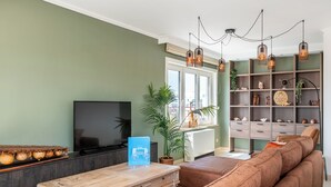 A living room with a sofa, a coffee table, a TV, and a bookshelf. - Beautiful penthouse flat with central location (Koksijde)