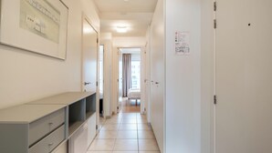 A hotel hallway with a desk, drawers, and a bed in the distance. - Cosy flat with frontal sea view (Koksijde)