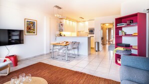 A modern living room with a flat-screen TV, a dining area with a table and chairs, a kitchen with white cabinets, and a bright red bookshelf. - Cosy flat with frontal sea view (Koksijde)