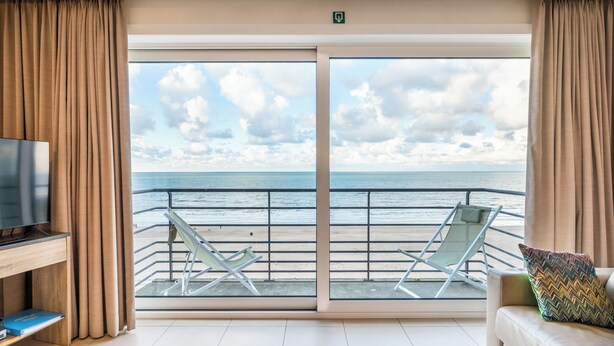 Une pièce dotée d’une grande porte-fenêtre coulissante donnant sur un balcon avec vue sur la mer et les nuages.