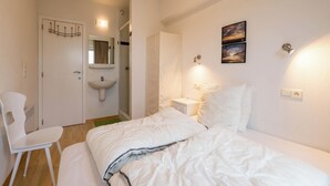 Une chambre à coucher comprenant un lit, une chaise, une table de chevet, une commode, une lampe fixée au mur, un miroir fixé au mur et un tableau.