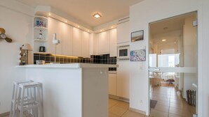 Une cuisine moderne avec des meubles blancs, un four à micro-ondes encastré et un petit îlot central avec des tabourets.