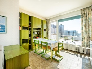 A room with a dining table and chairs, green cabinets, and a view of a building through a large window.