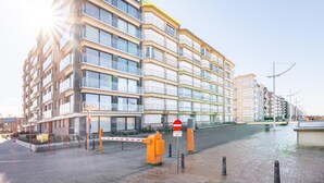 Un edifici residencial de diversos pisos amb balcons, una entrada tancada amb reixeta i un cel serè.