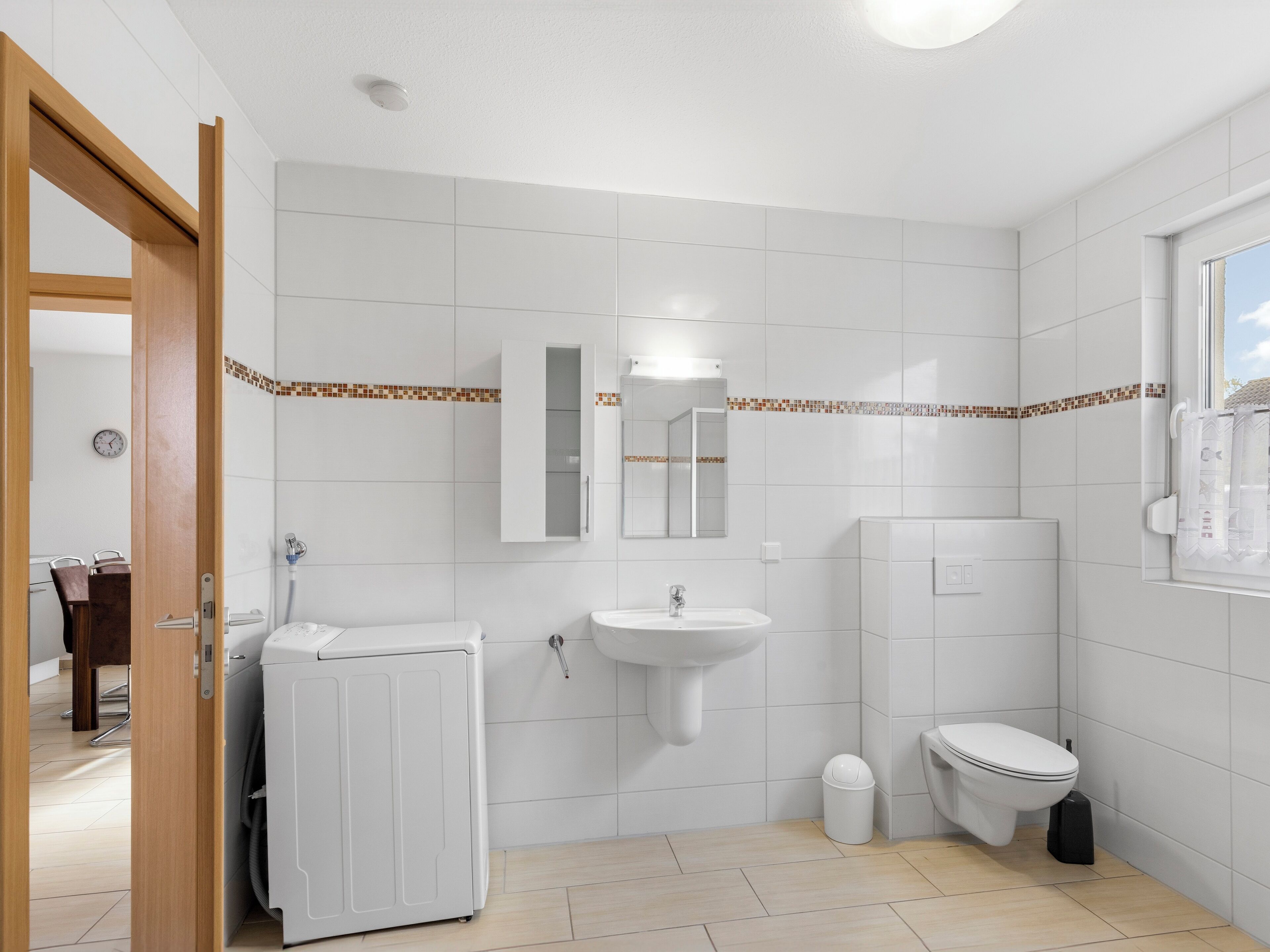 A modern bathroom with a white sink, toilet, and washing machine.