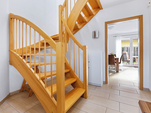 A wooden staircase leading to an upper floor, a white door, and a view of an outdoor patio area with a table and chairs.