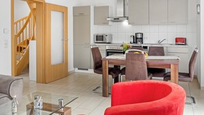 A modern kitchen with white cabinets, a wooden dining table, and a red chair. A staircase leads to a second floor. - Cosy holiday home ideal for 2 families (Boiensdorf)