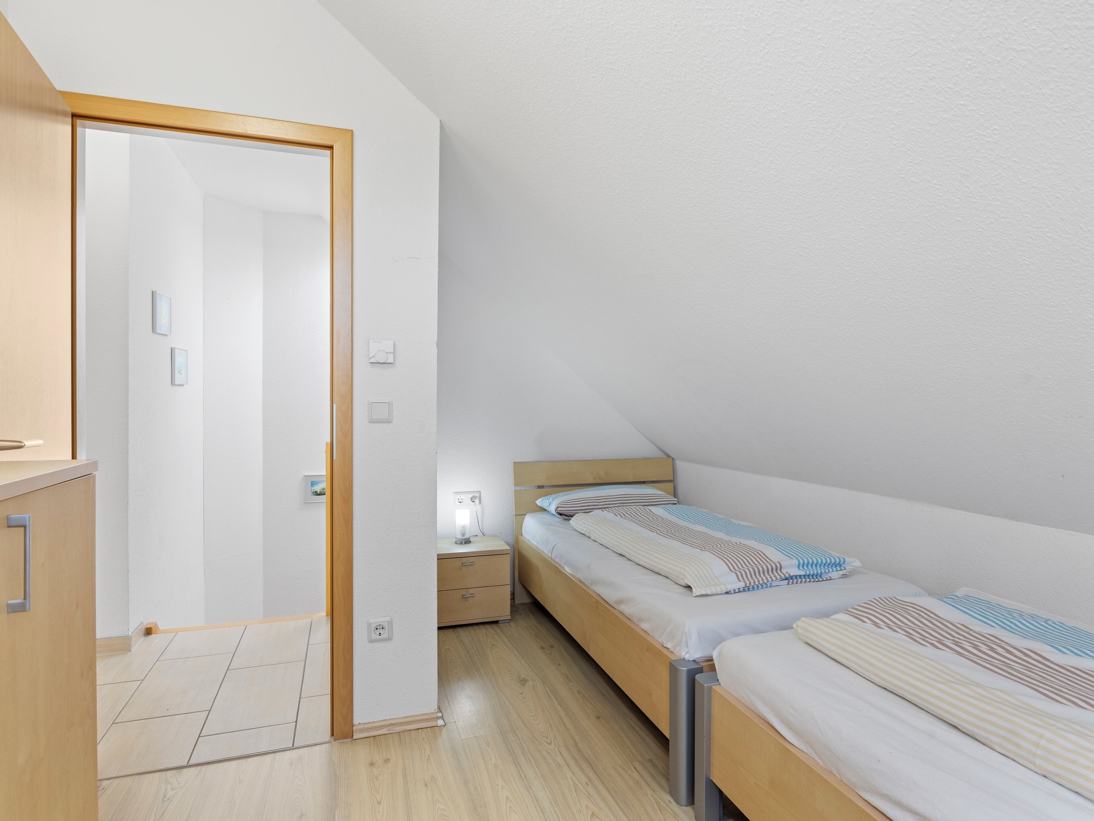 A bedroom with two single beds, a nightstand, a bedside table, and a wooden wardrobe.