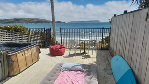 Une terrasse en bois avec un matelas, un pouf rouge et une planche de surf bleue.