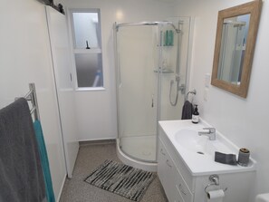 A modern bathroom with a glass shower enclosure, a white sink with a mirror, and a towel rack.